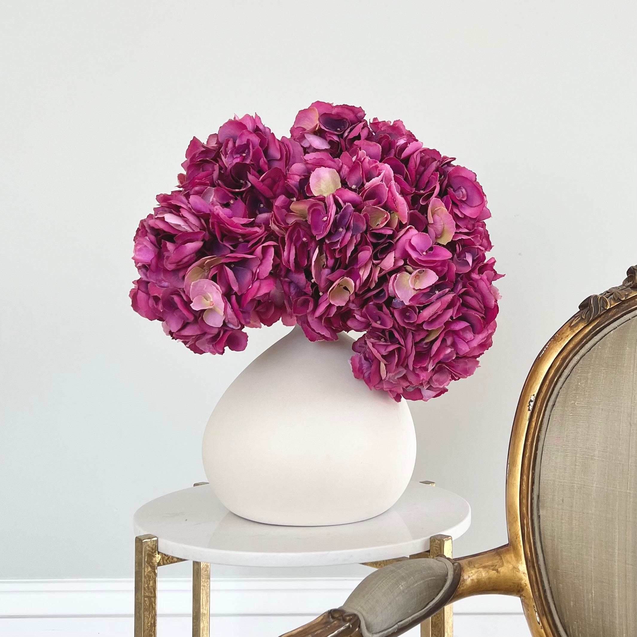Luxury Lifelike Realistic Artificial Fabric Silk Blooms with Foliage Buy Online from The Faux Flower Company | 7 stems of Fuchsia Mophead Hydrangea ABY8306FP styled in Ceramic Matte White Burford Vase ABP1747